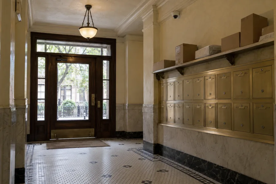 Dome camera on the ceiling above brass mailboxes and a package shelf in an apartment lobby